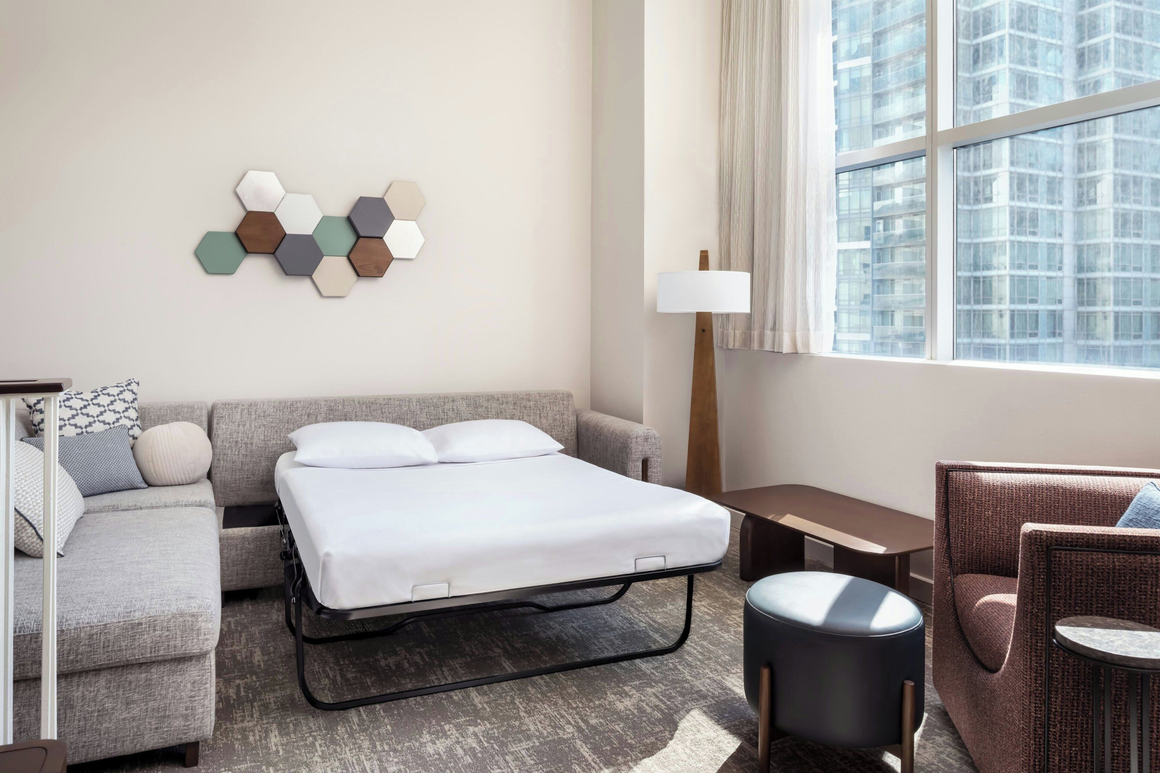 Una habitación de hotel con cama, sofá, sillón, una mesita y una lámpara.