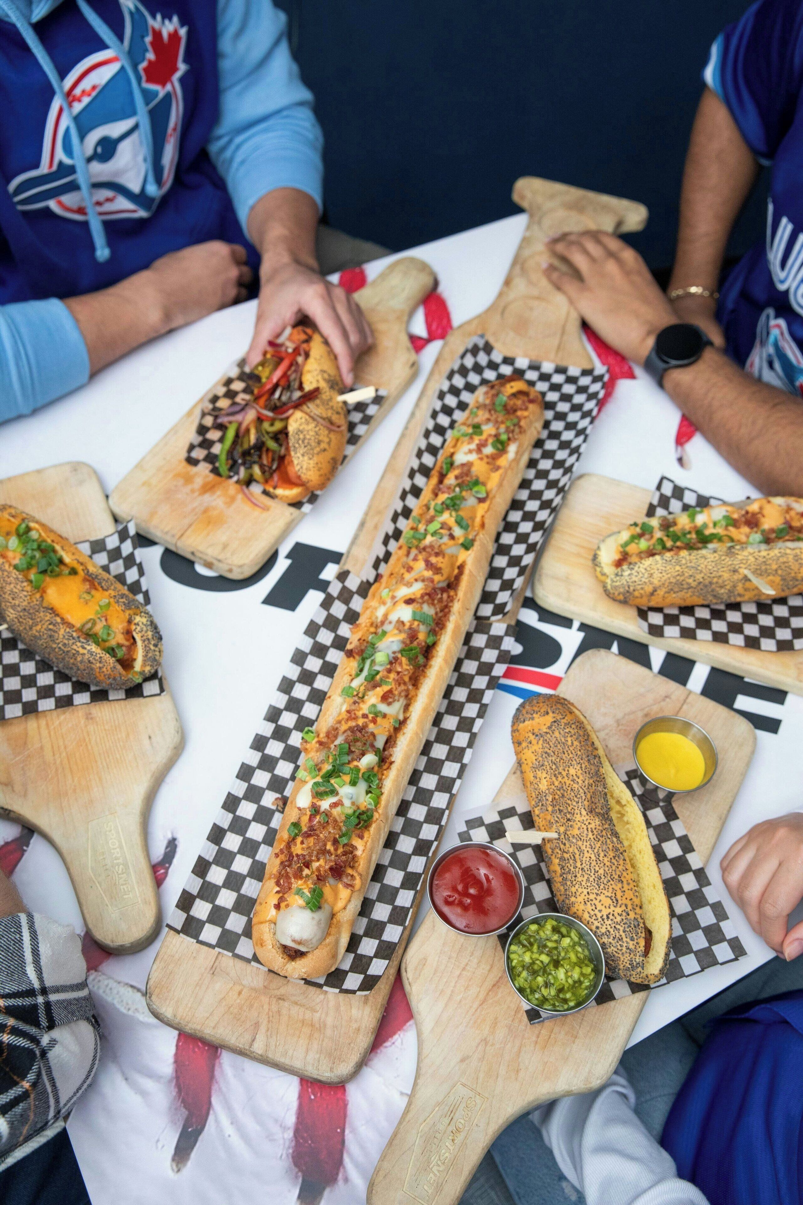 Una mesa larga con diversos alimentos, como sándwiches y salsas, sobre un mantel a cuadros.