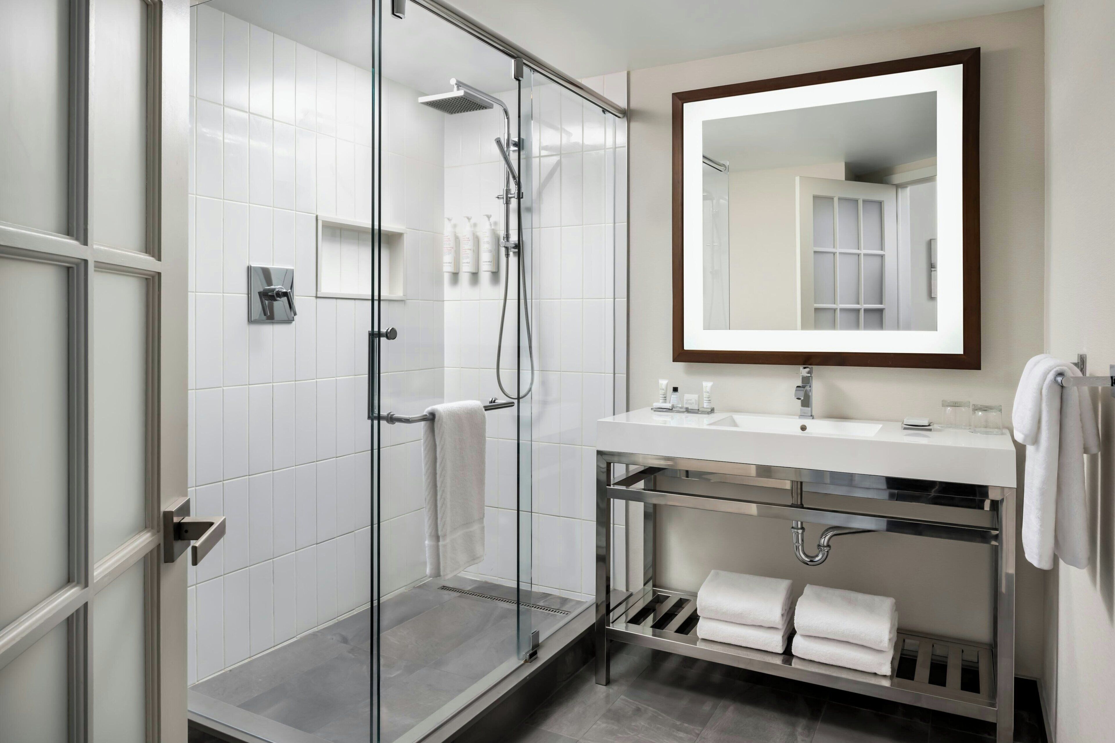 Un baño moderno con cabina de ducha de vidrio, un lavabo blanco con espejo y un perchero para toallas.
