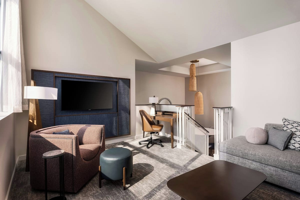 Et moderne hotelværelse med et fladskærms-tv, en sofa, et skrivebord og en stol.