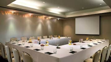 Una sala de conferencias con una larga mesa, sillas, una pantalla de proyector y una pizarra.