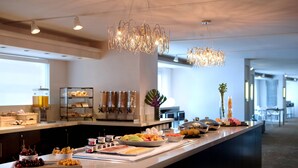 A buffet setup with various food items and a modern chandelier.