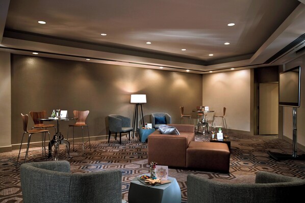 Un hall de hotel con un área de estar que incluye sofás y sillones, una mesita con lámpara, y una alfombra estampada.