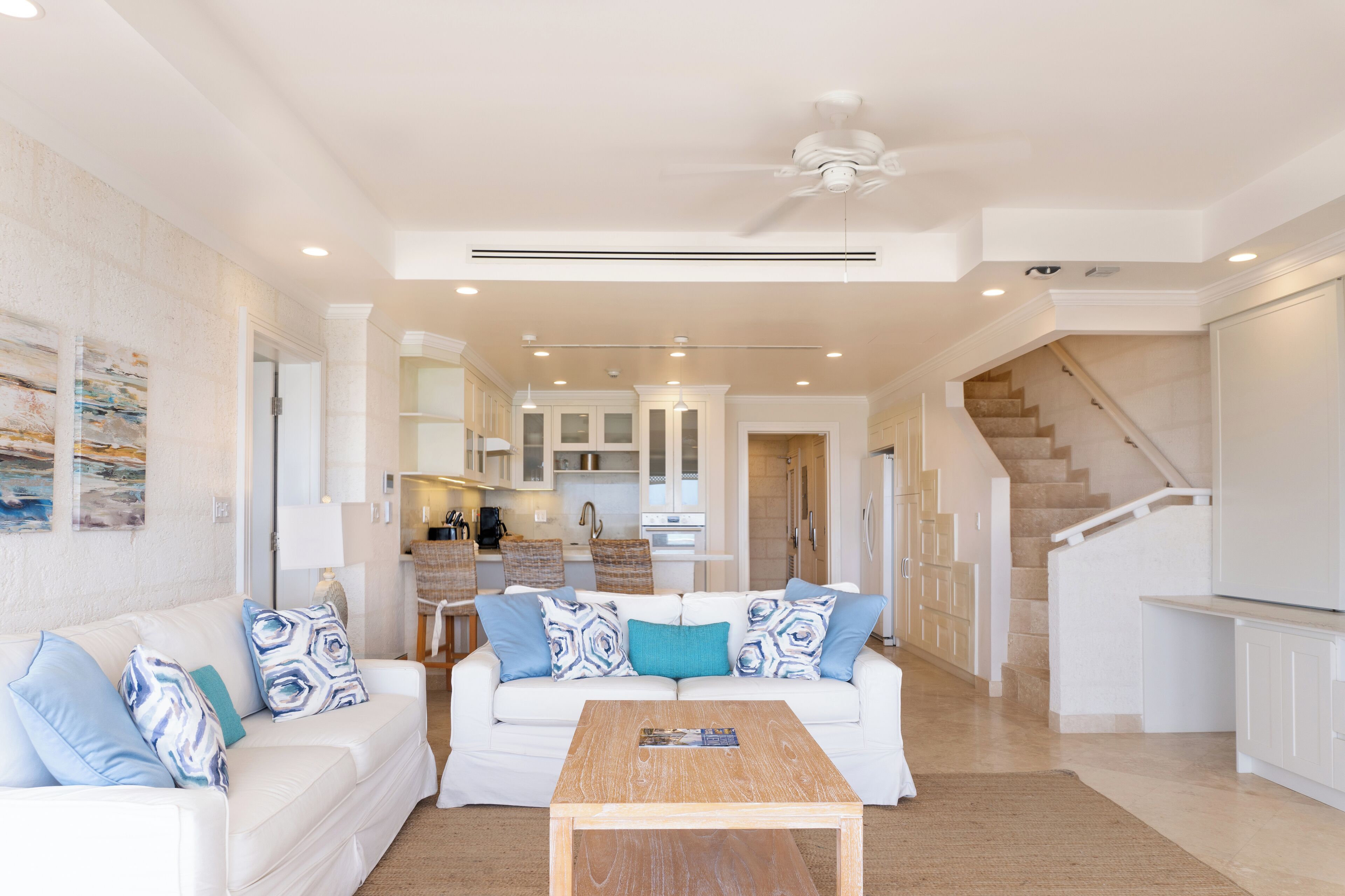 A spacious living area with a white sofa, a wooden coffee table, and a kitchen in the background.