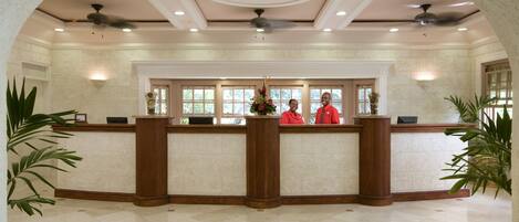 A reception area with a marble floor, a reception desk, and two staff members in red uniforms.