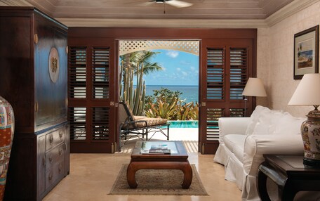 A room with a view of the ocean, a white sofa, a wooden coffee table, and a ceiling fan.