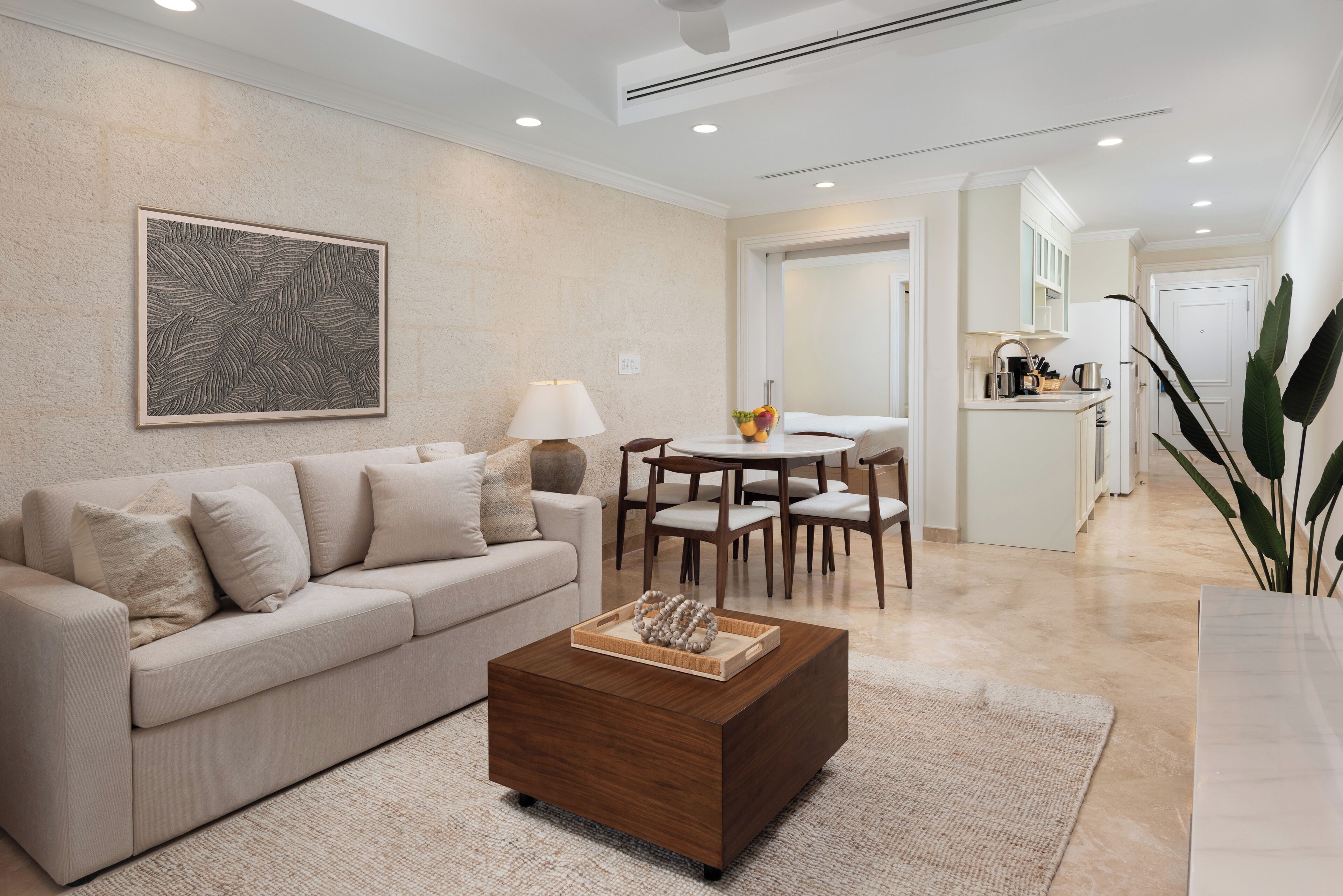 A modern living room with a beige sofa, a wooden coffee table, and a dining area with a white table and chairs.