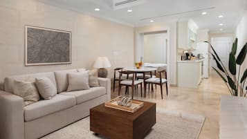 A modern living room with a beige sofa, a wooden coffee table, and a dining area with a white table and chairs.