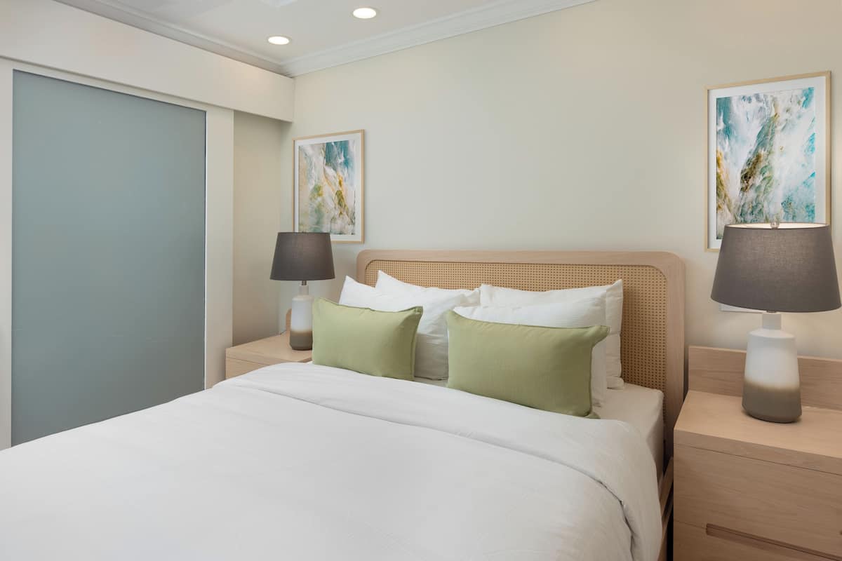 Habitación de hotel con una cama, dos mesitas de noche, una lámpara y dos cuadros en la pared.