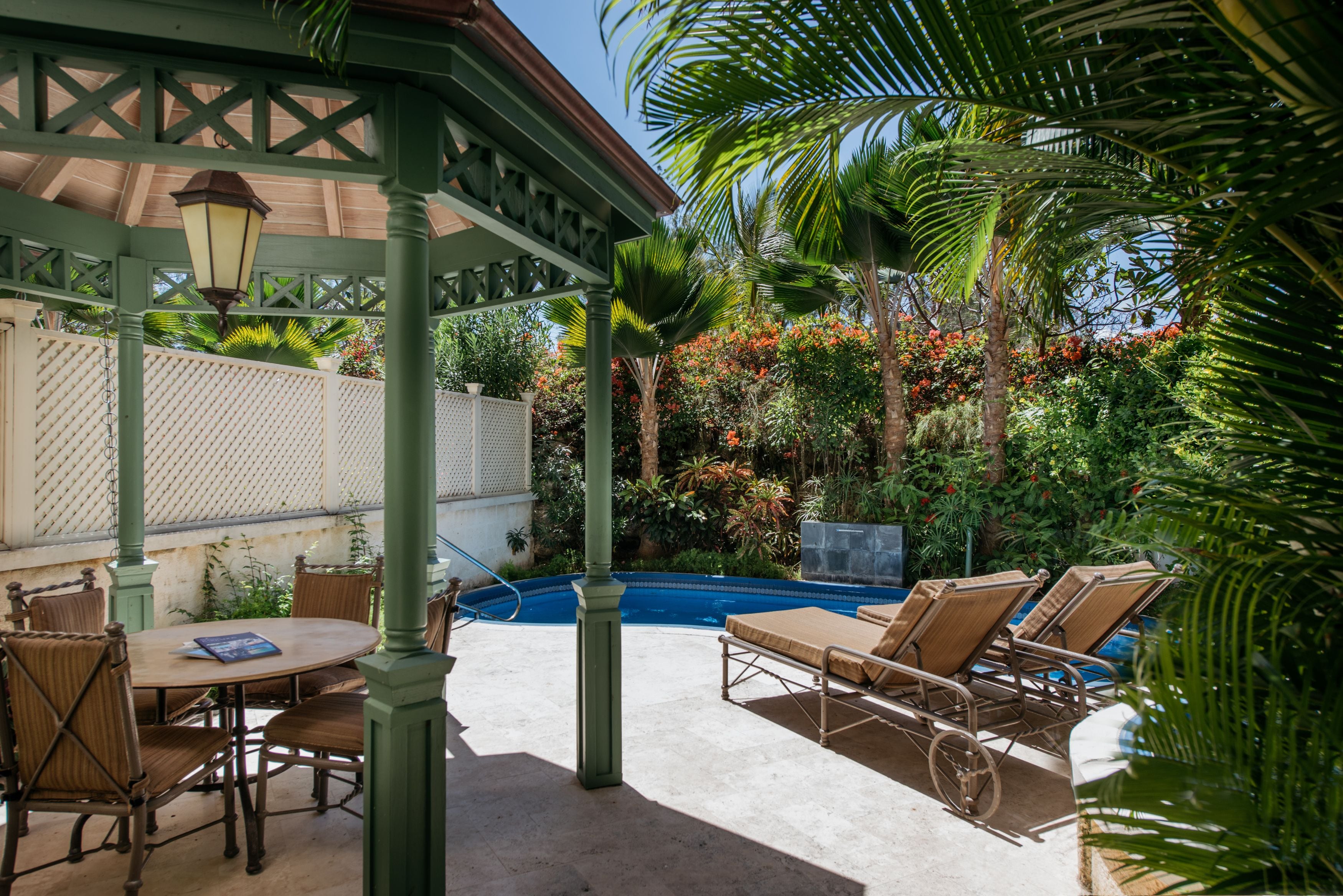 Un patio techado con piscina, sillones de descanso y una mesa con sillas.