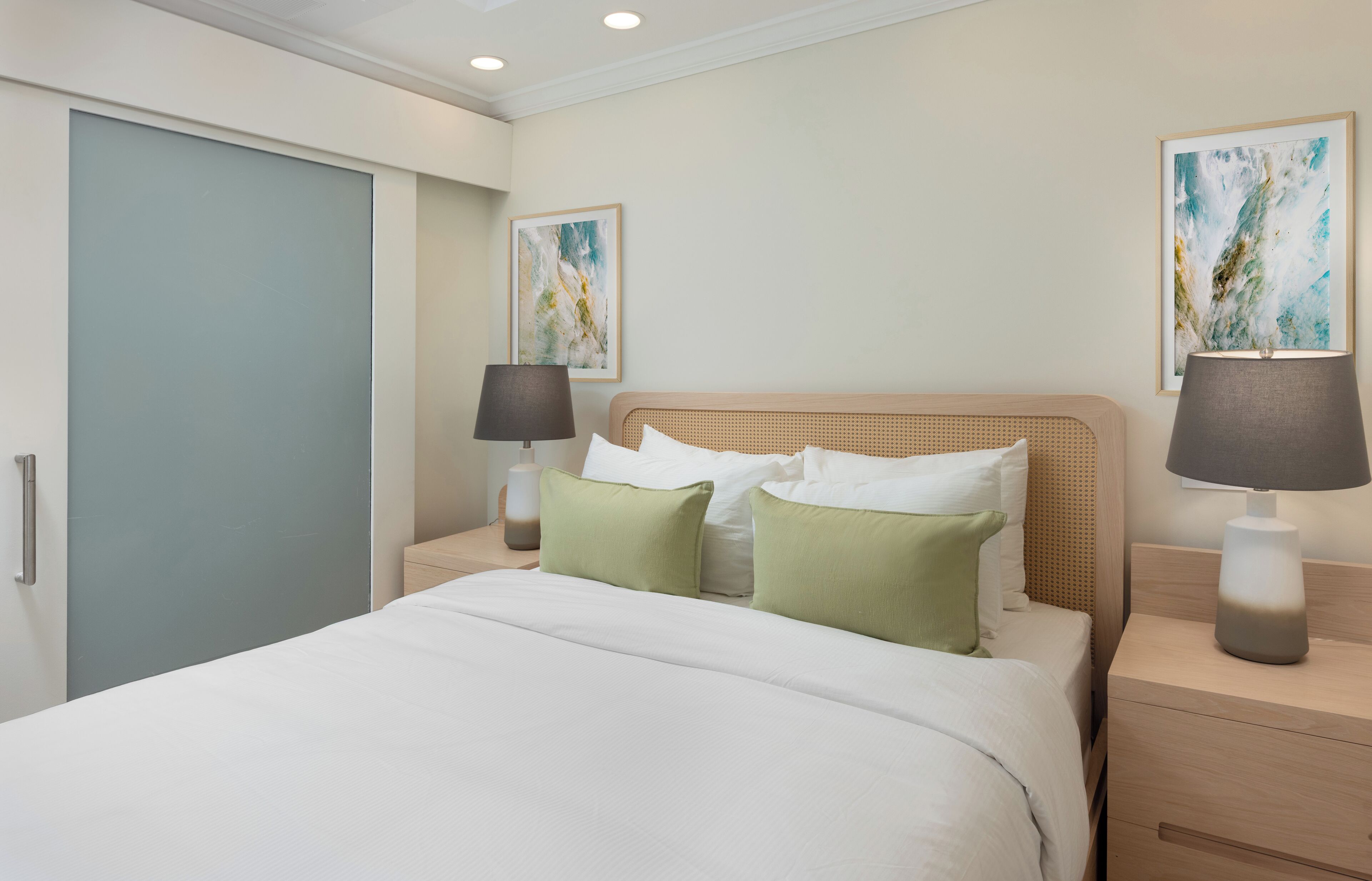 A hotel room with a bed, two bedside tables, a nightstand, a lamp, and two framed pictures on the wall.