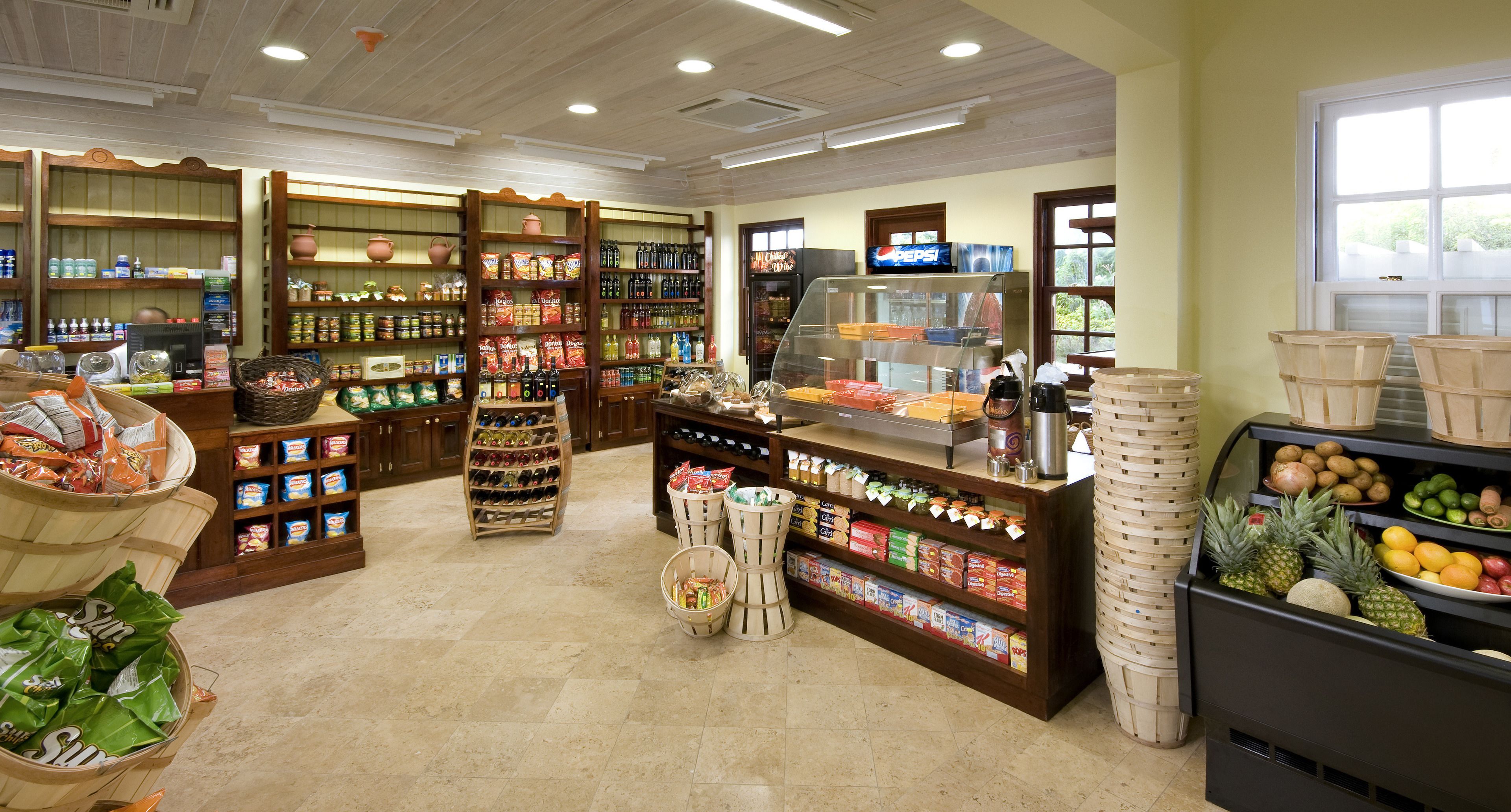 A grocery store interior with shelves stocked with various food items, a display counter, and baskets of produce.