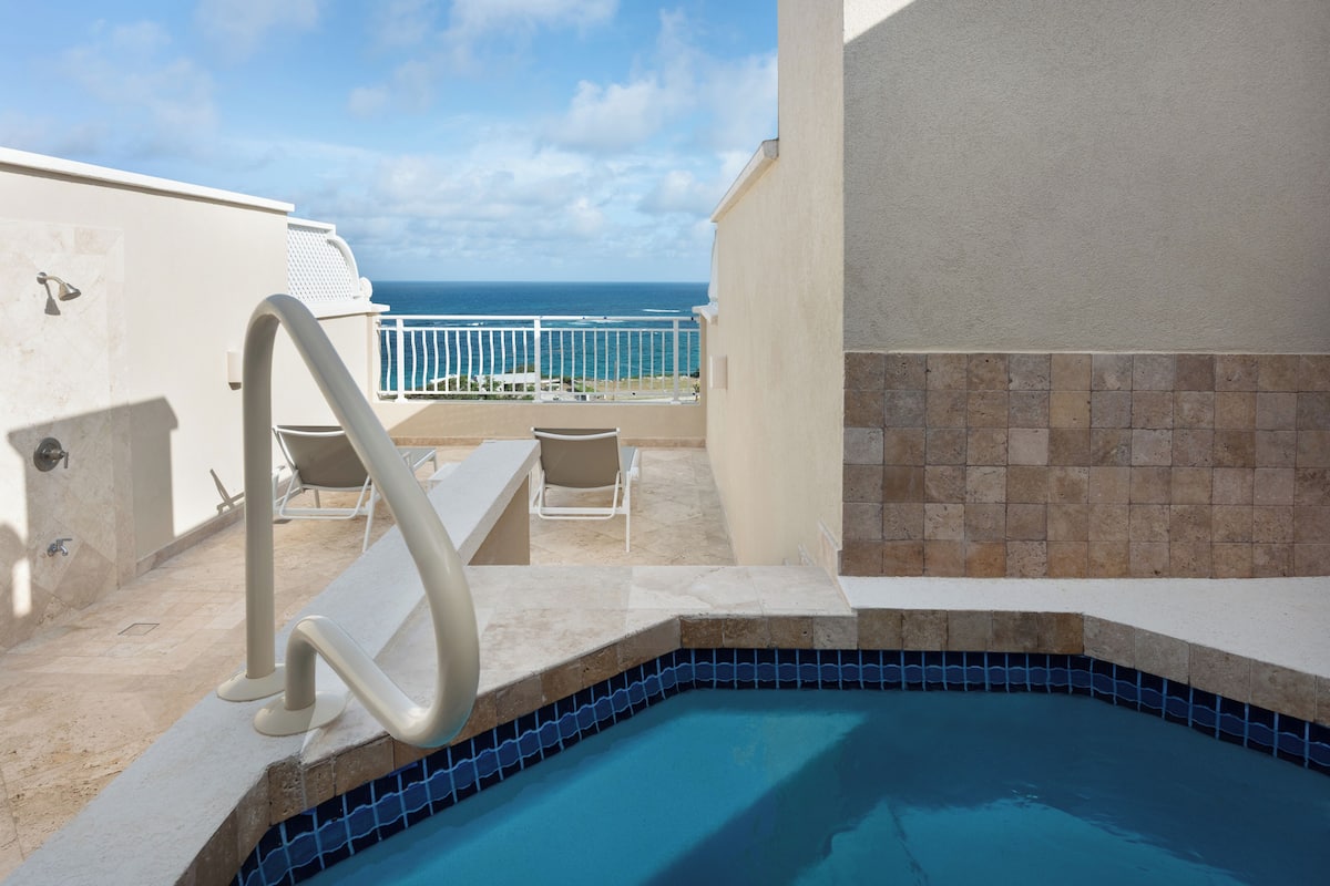 Zona de piscina con vistas al océano, una silla blanca y una mesita.