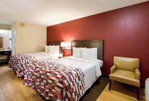 Una habitación de hotel con dos camas, una silla y una mesita de noche con lámpara.