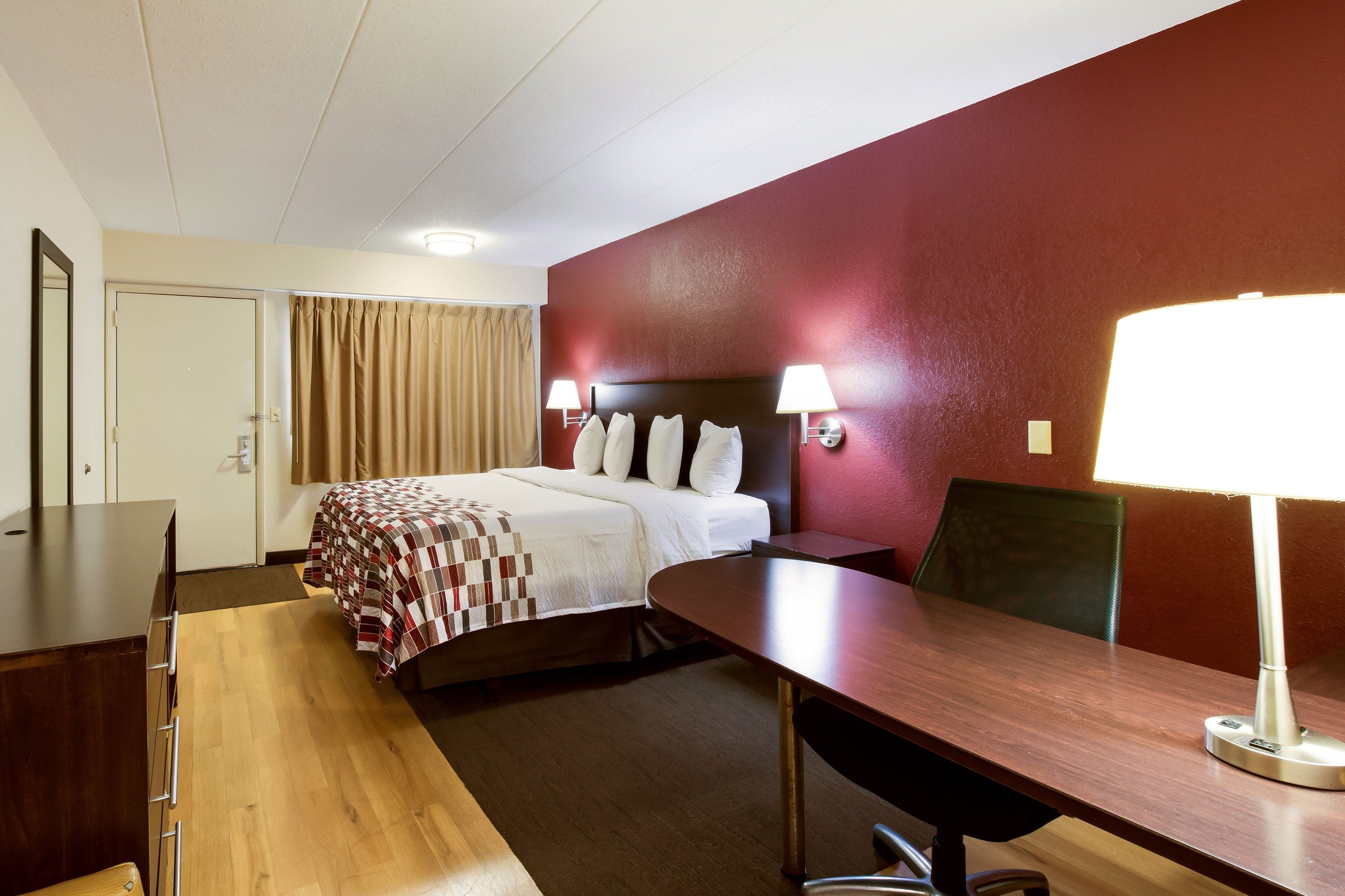 Une chambre d’hôtel avec un lit, un bureau, une chaise, une lampe et une porte.