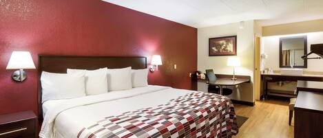 Une chambre d’hôtel avec un lit, des lampes de chevet, un bureau, une chaise, un miroir et un tableau au mur.