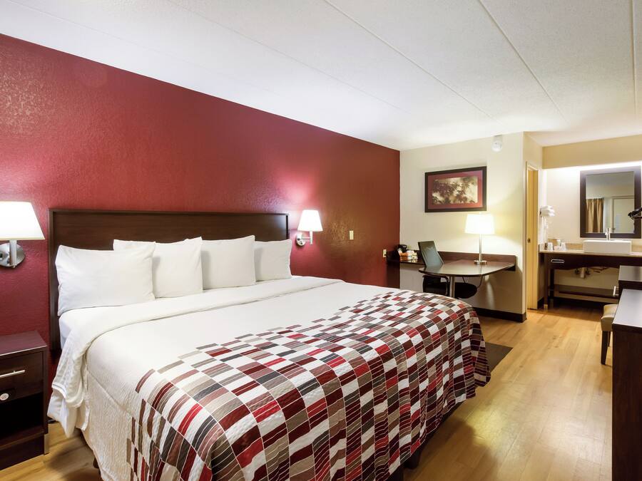 A hotel room with a bed, bedside lamps, a desk, a chair, a mirror, and a painting on the wall.