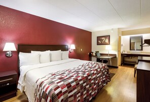 Habitación de hotel con cama, lámparas de noche, escritorio, silla, espejo y un cuadro en la pared.