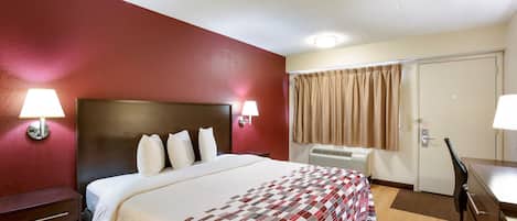 A hotel room with a bed, bedside lamps, a desk, and a window with curtains.