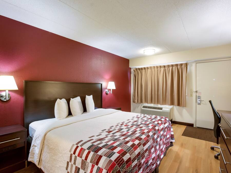 A hotel room with a bed, bedside lamps, a desk, and a window with curtains.