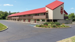 A motel with a red roof and beige walls, featuring a parking lot and a landscaped area with shrubs. - Red Roof Inn Kalamazoo East - Expo Center (Kalamazoo)