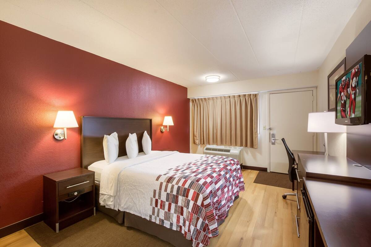 A hotel room with a bed, bedside lamps, a desk, and a television.