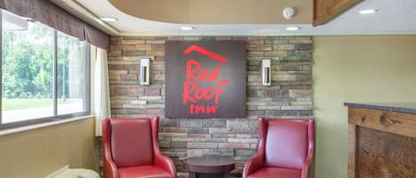 A Red Roof Inn reception area with two leather chairs, a stone wall, and a small round table.