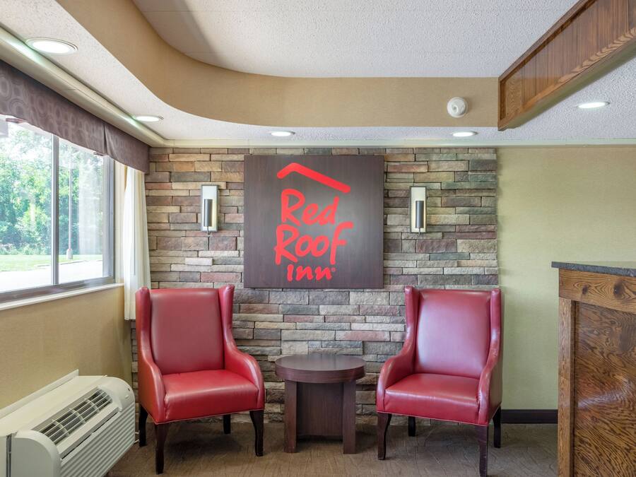 A Red Roof Inn reception area with two leather chairs, a stone wall, and a small round table.