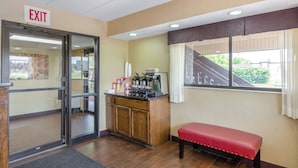 A hotel lobby with an exit sign, a coffee machine, a bench, and a window with a view of a building. - Red Roof Inn Kalamazoo East - Expo Center (Kalamazoo)