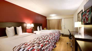 A hotel room with three beds, a desk, a television, and a window with curtains.
