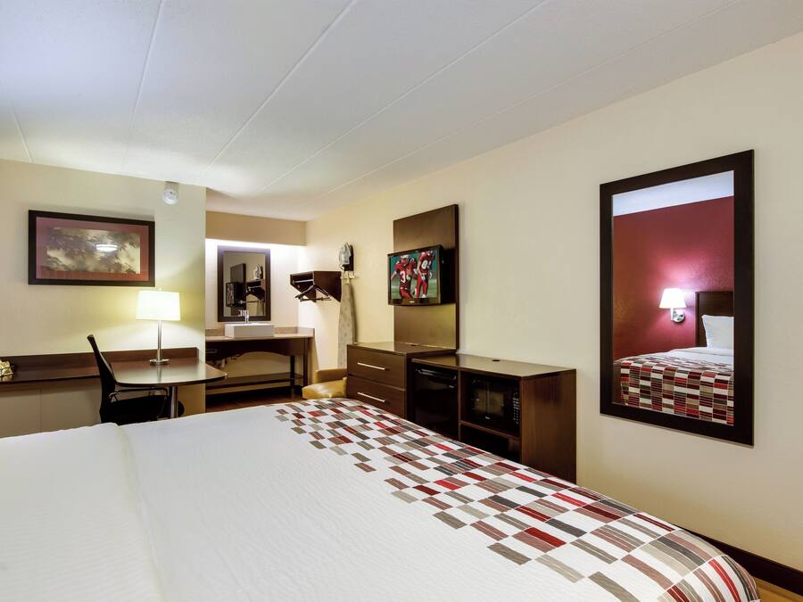 A hotel room with a bed, desk, chair, and a large mirror.