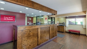 A reception area with a wooden reception desk, a red sign indicating free Wi-Fi, a clock, and a coffee machine. - Red Roof Inn Kalamazoo East - Expo Center (Kalamazoo)