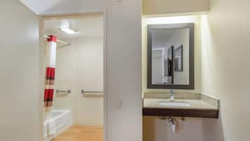 Et badeværelse med badekar, bruseforhæng, håndvask med spejl og toilet.