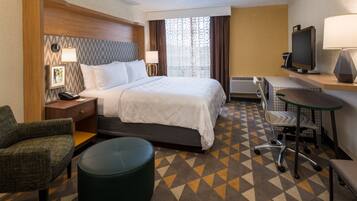 A hotel room with a bed, a desk, a chair, a television, and a patterned carpet.