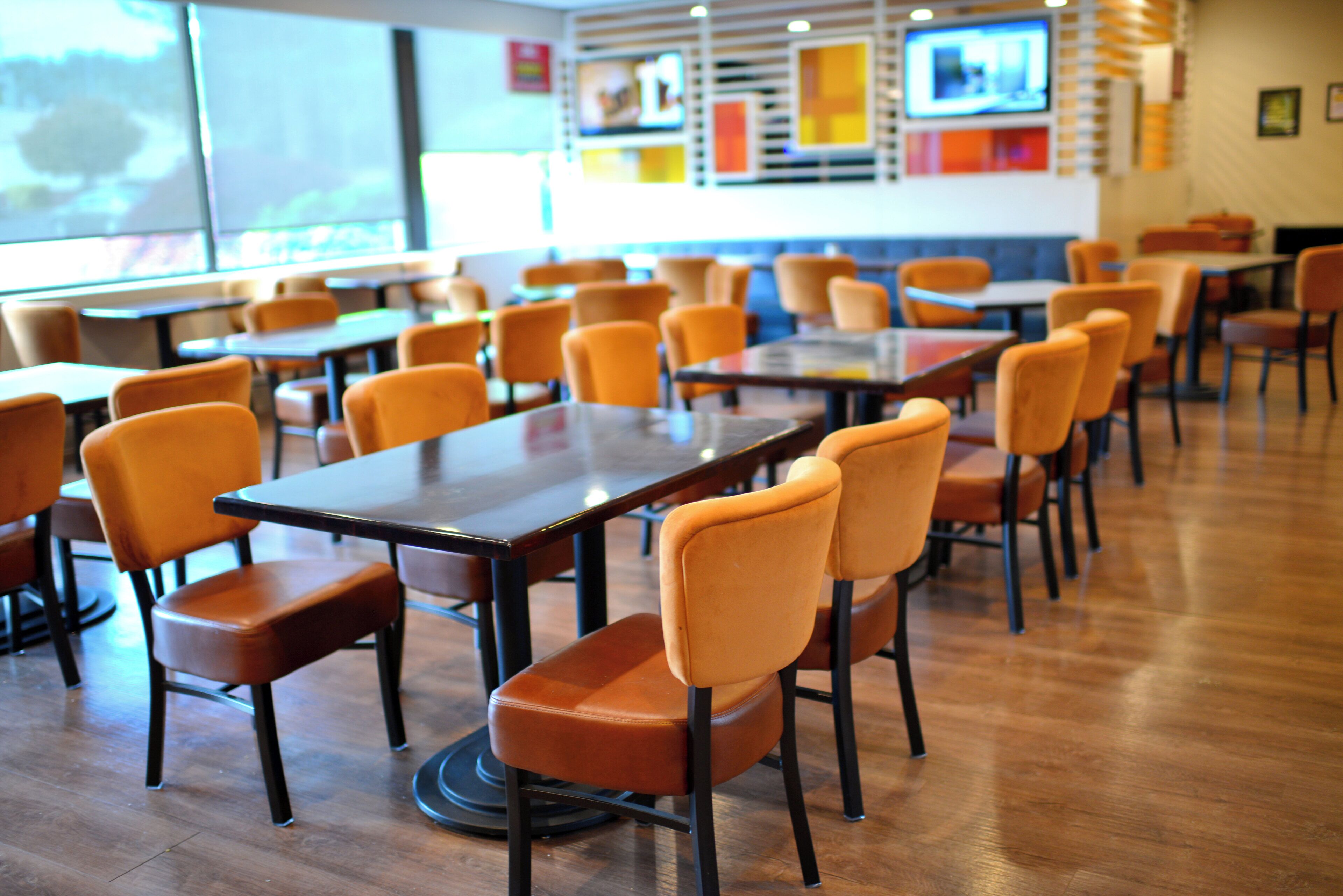 Interior de un restaurante con varias mesas y sillas, suelo de madera y un ventanal grande al fondo.