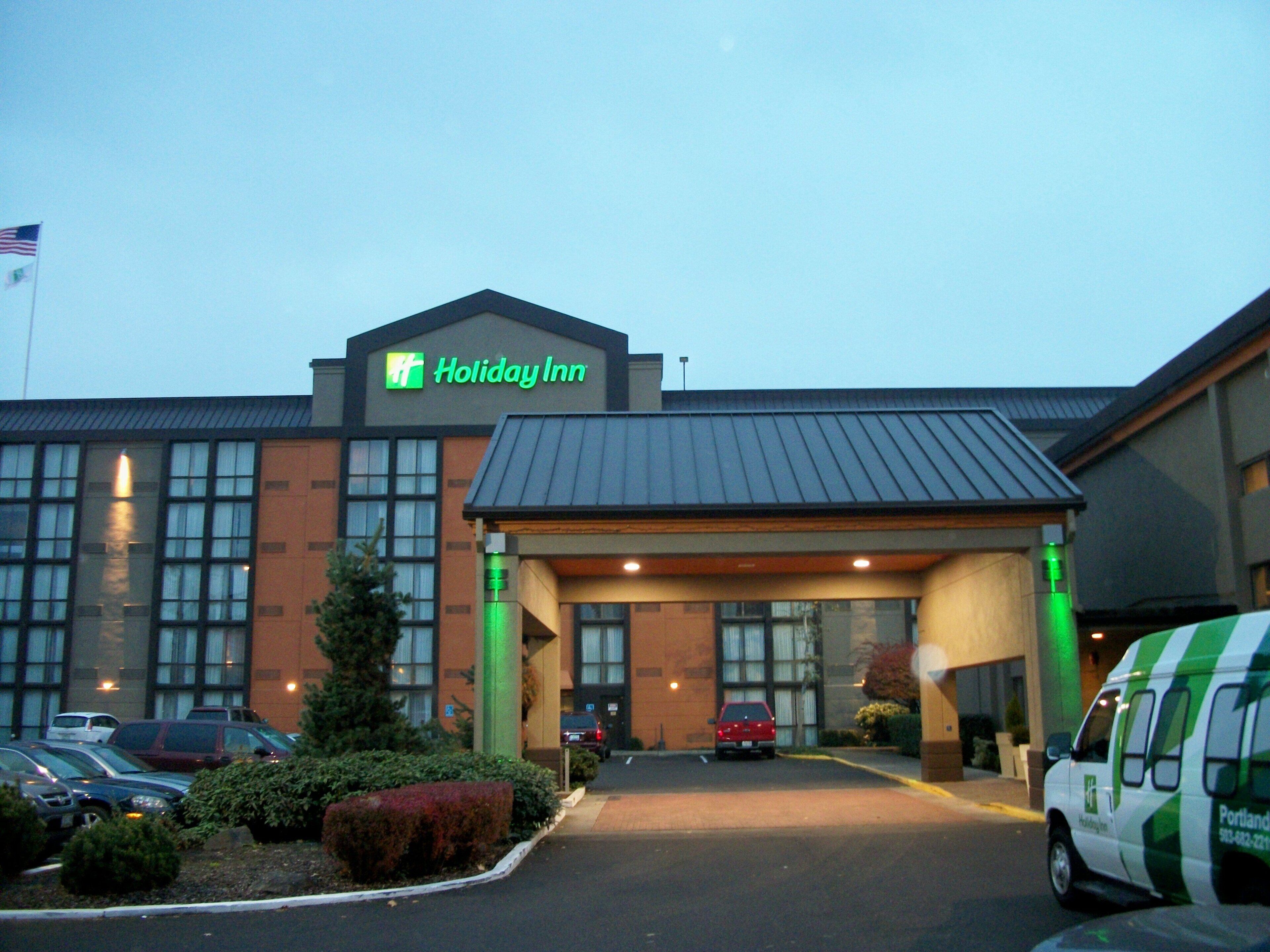 A Holiday Inn hotel with a large entrance, parking lot, and a flag in the background.