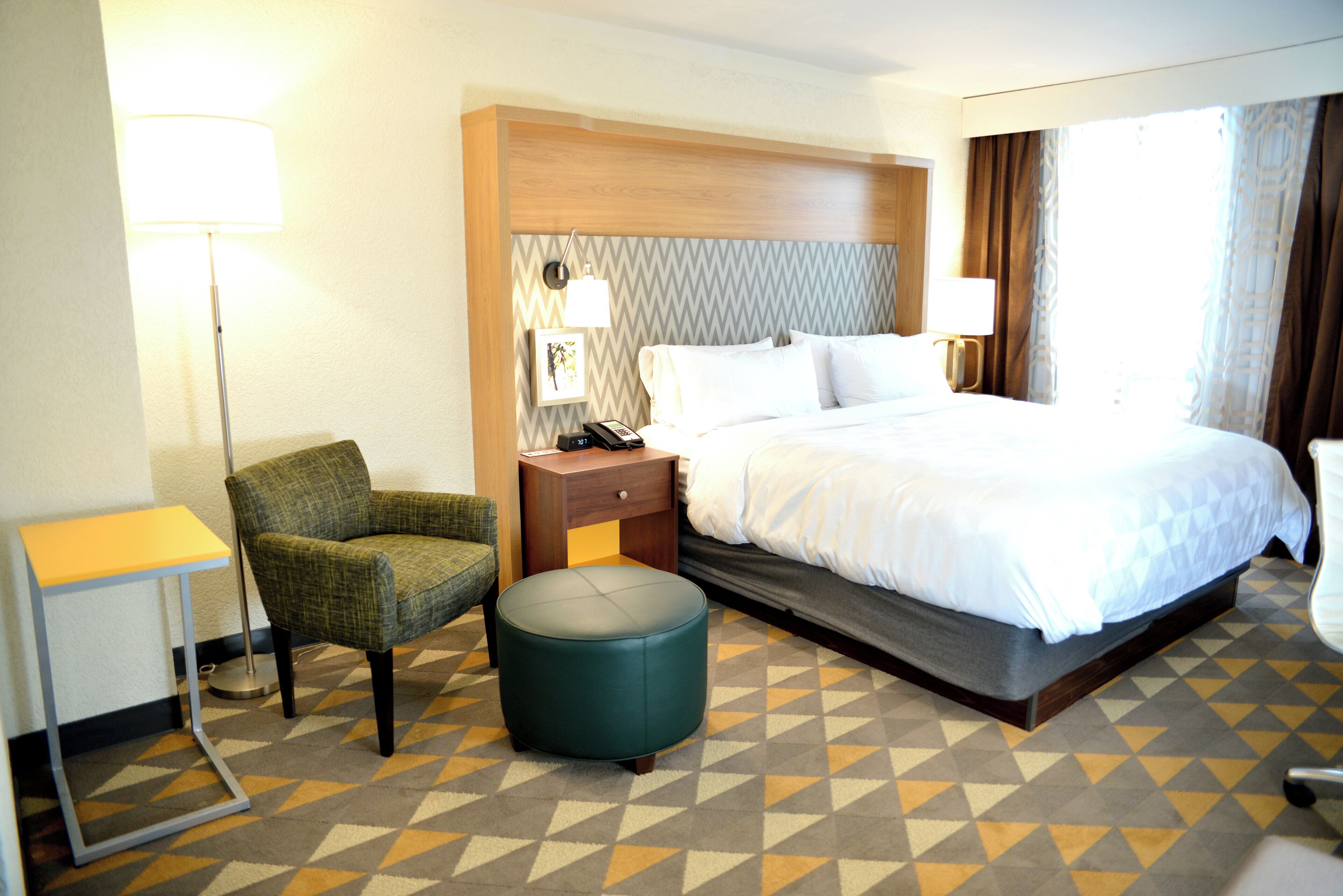 Ein Hotelzimmer mit Bett, Stuhl, Nachttisch, Lampe und einem gemusterten Teppich.