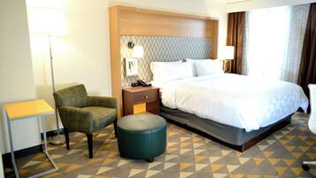 Ein Hotelzimmer mit Bett, Stuhl, Nachttisch, Lampe und einem gemusterten Teppich.