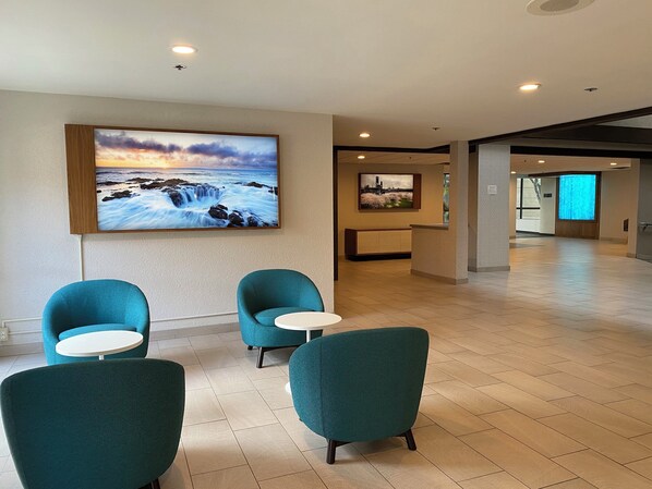 A lobby with teal chairs, a reception desk, and a large painting of a seascape.