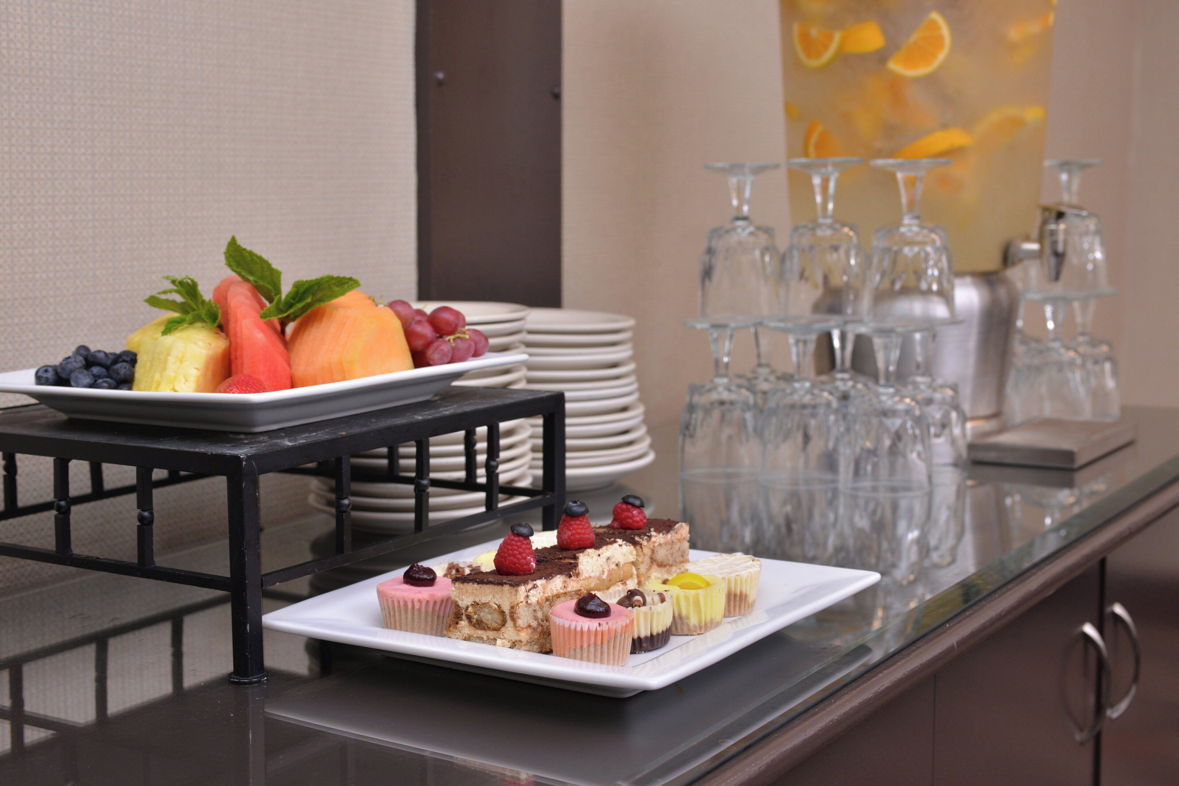 A buffet table with various desserts and fruits, a stack of plates, and a glassware arrangement.