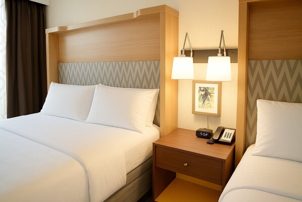 Quarto de hotel com uma cama grande, mesa de cabeceira com abajur, telefone e porta-retrato.