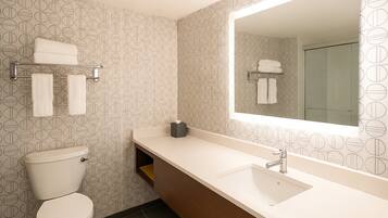 A modern bathroom with a toilet, a sink, and a mirror. There are towels on the wall and a shelf with towels.