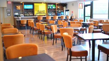 A restaurant with multiple tables and chairs, a bar area with a television screen, and a window providing natural light.