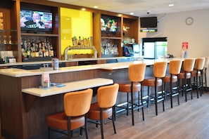 A bar area with a counter, multiple stools, and a television screen displaying a program.