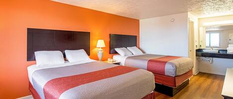 Ein Hotelzimmer mit zwei Betten, einem Nachttisch mit Lampe und einem durchgegangenen Tür sichtbaren Badezimmer.
