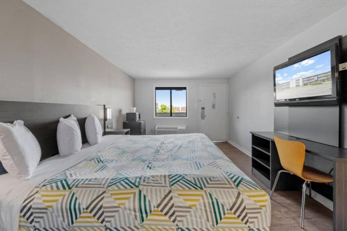 A hotel room with a bed, a desk, a chair, a TV, and a window.
