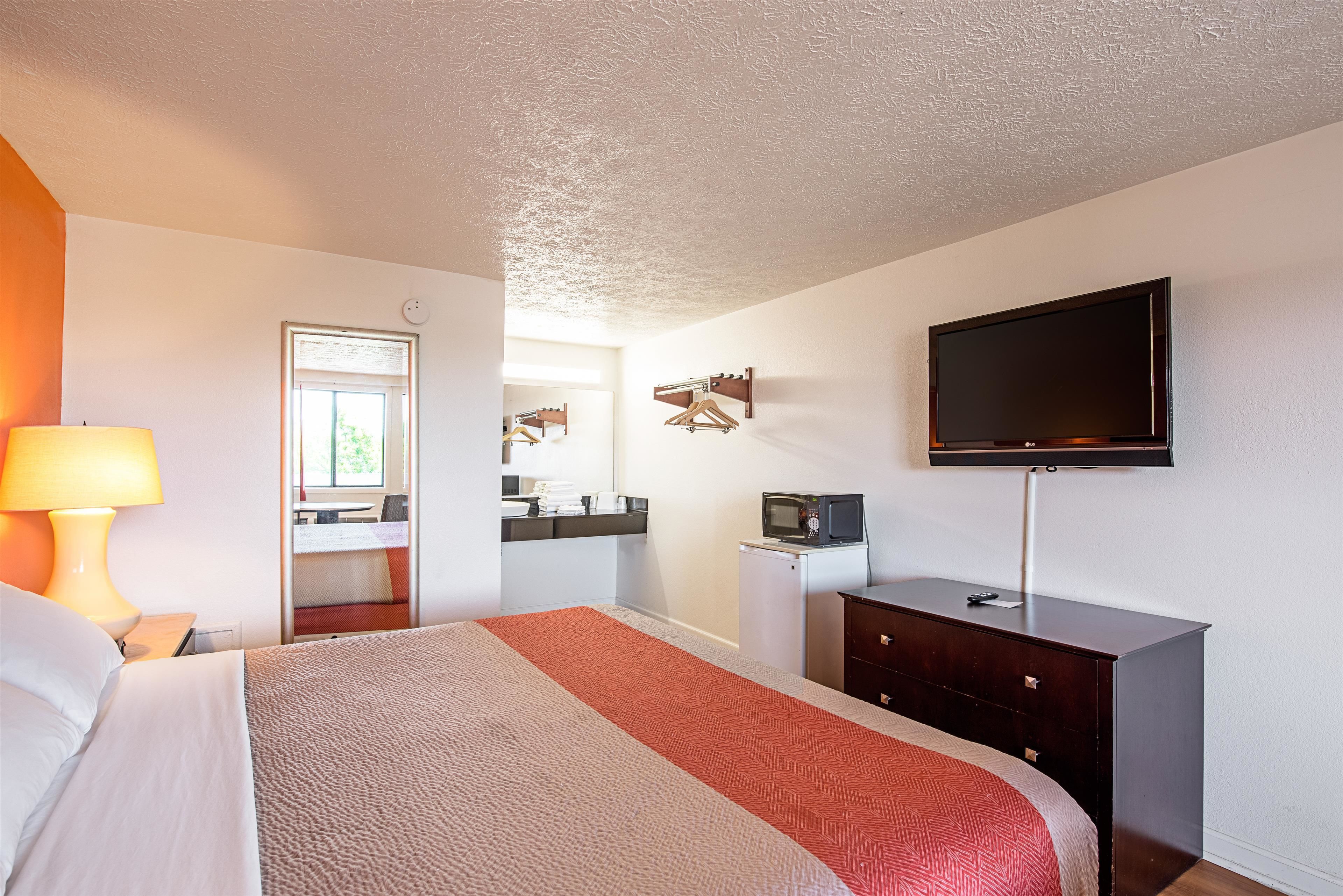 Une chambre d’hôtel comprenant un lit, un bureau avec une lampe, une télévision, une commode et un miroir.