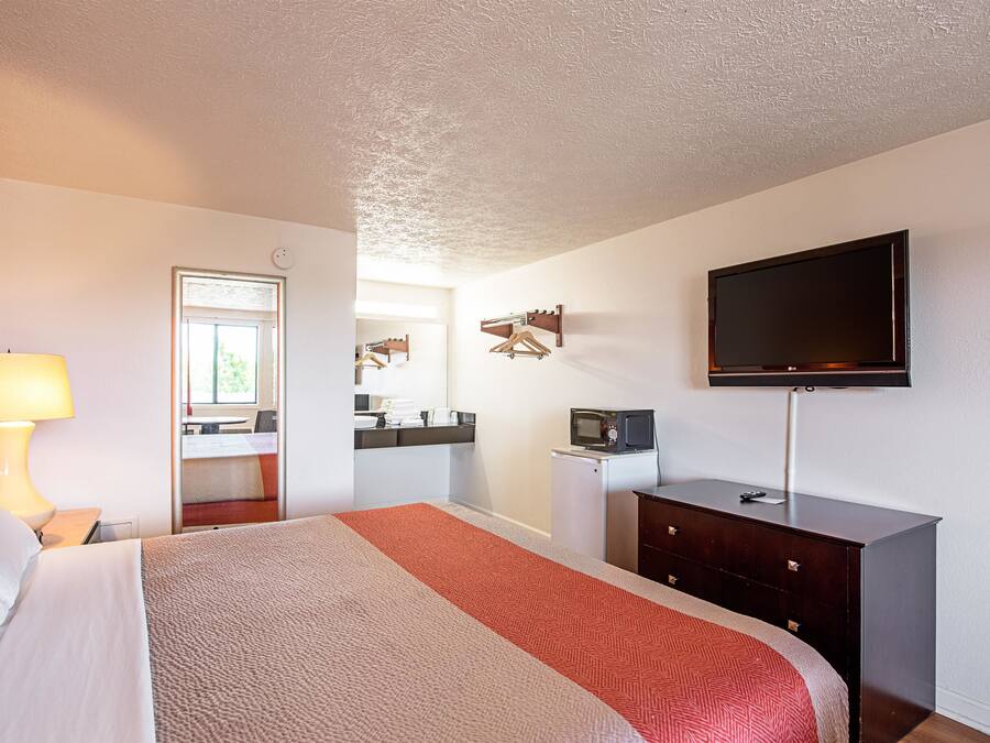 Une chambre d’hôtel comprenant un lit, un bureau avec une lampe, une télévision, une commode et un miroir.