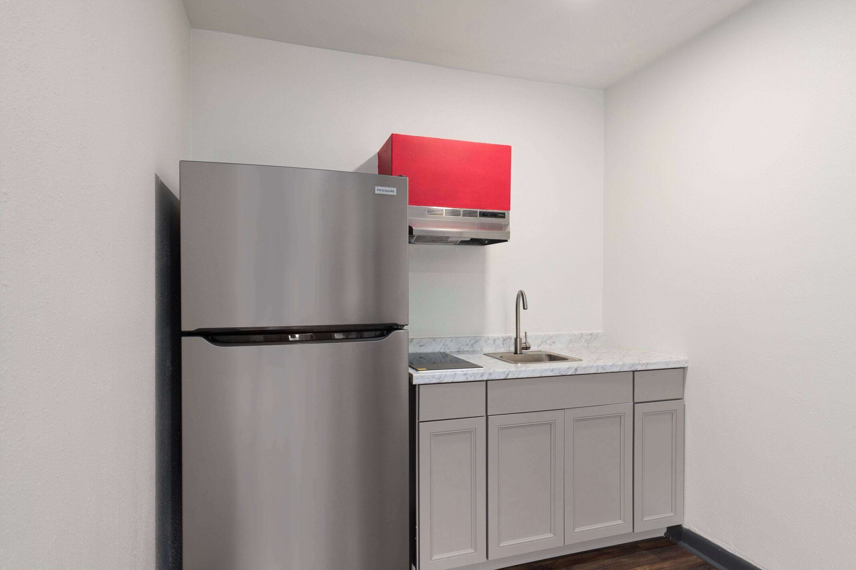A kitchen with a stainless steel refrigerator, a red upper cabinet, a sink, and light grey cabinets.