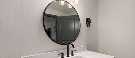 Un baño con lavamanos de mármol blanco, un espejo redondo y una lámpara de pared.